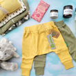 Load image into Gallery viewer, Two adorable pairs of baby harem pants in olive and light yellow are in the middle with other baby clothes, bath products, stuffy and chocolate around.