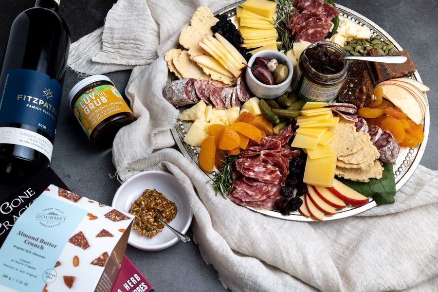 On a dark background, the local charcuterie and cheese box is plated beautifully with spreads, olives, chocolates, crackers, wine and more.