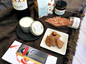 A closeup of open indulgent products, including local red wine, luxury candle, body butter, bath salts, and chocolate items.