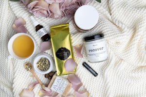 On a textured white blanket, the products within the wellness spa box gift are laid out including wellness tea from granville island tea co, french lavender scrub, hand sanitizer, bath soak and more. 